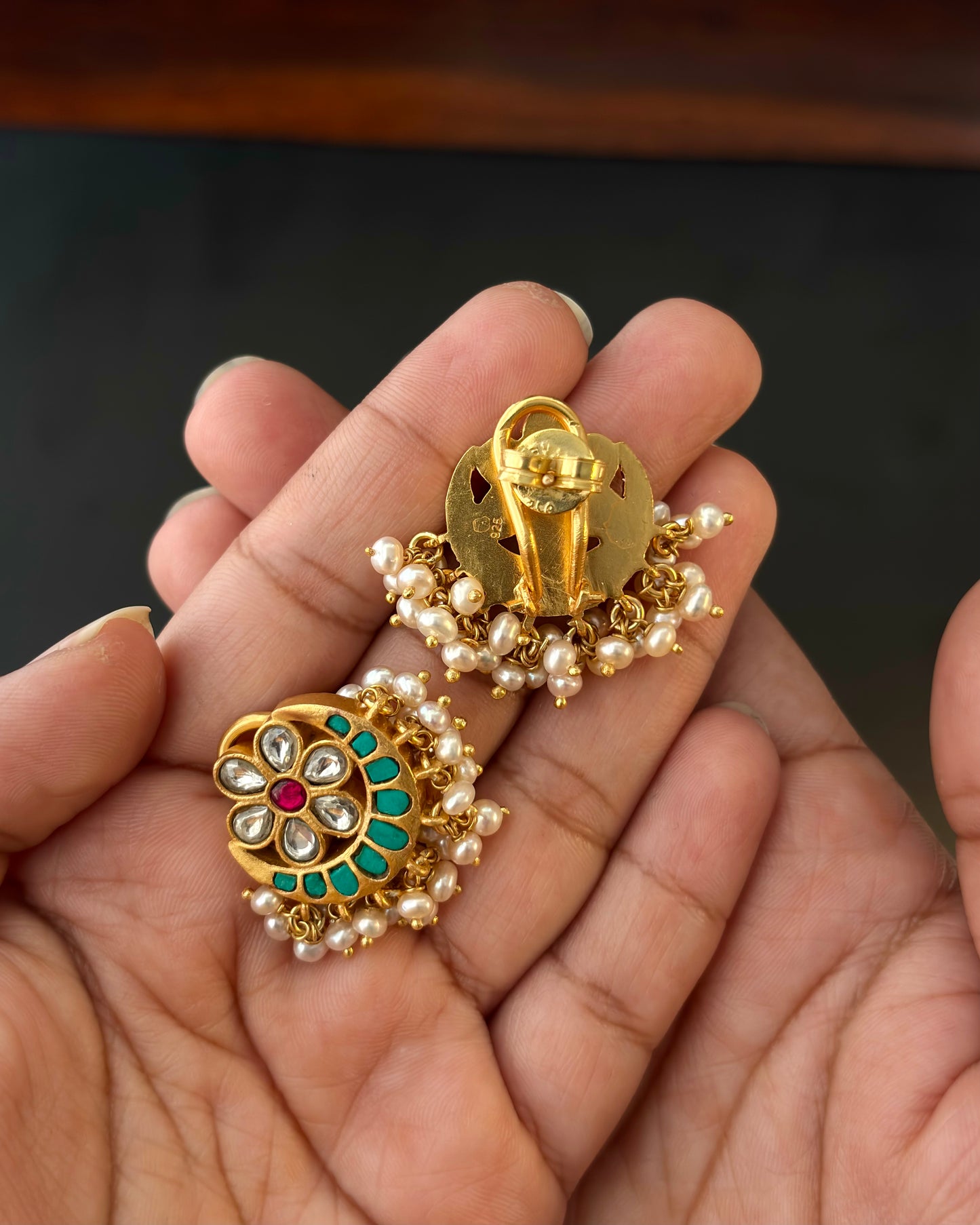 Gold earrings with pearls held in a hand against a dark background