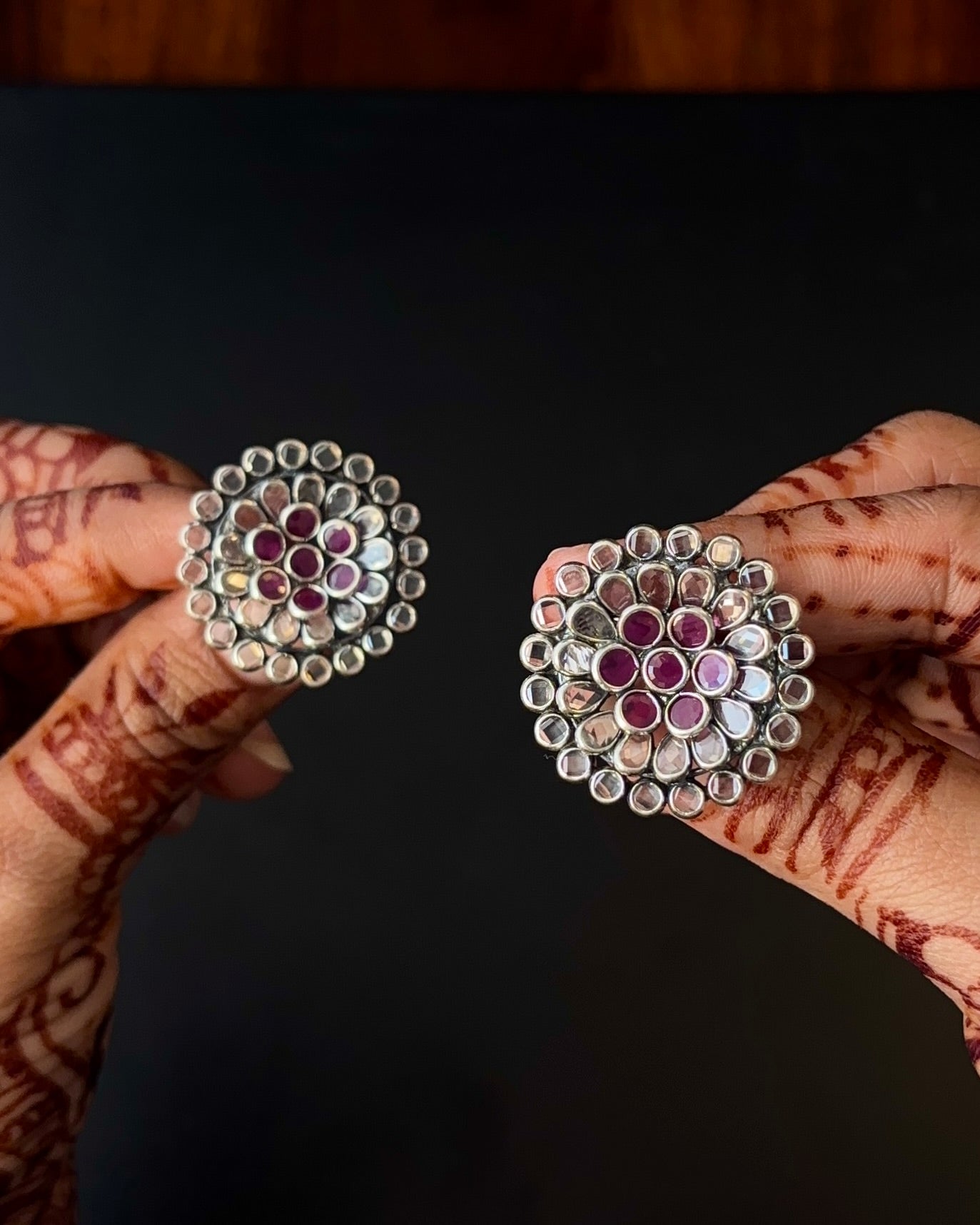 Pair of silver earrings with gemstones held by a hand against a dark background