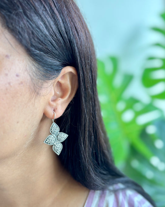 Close-up of a person wearing silver earrings with a blurred green background