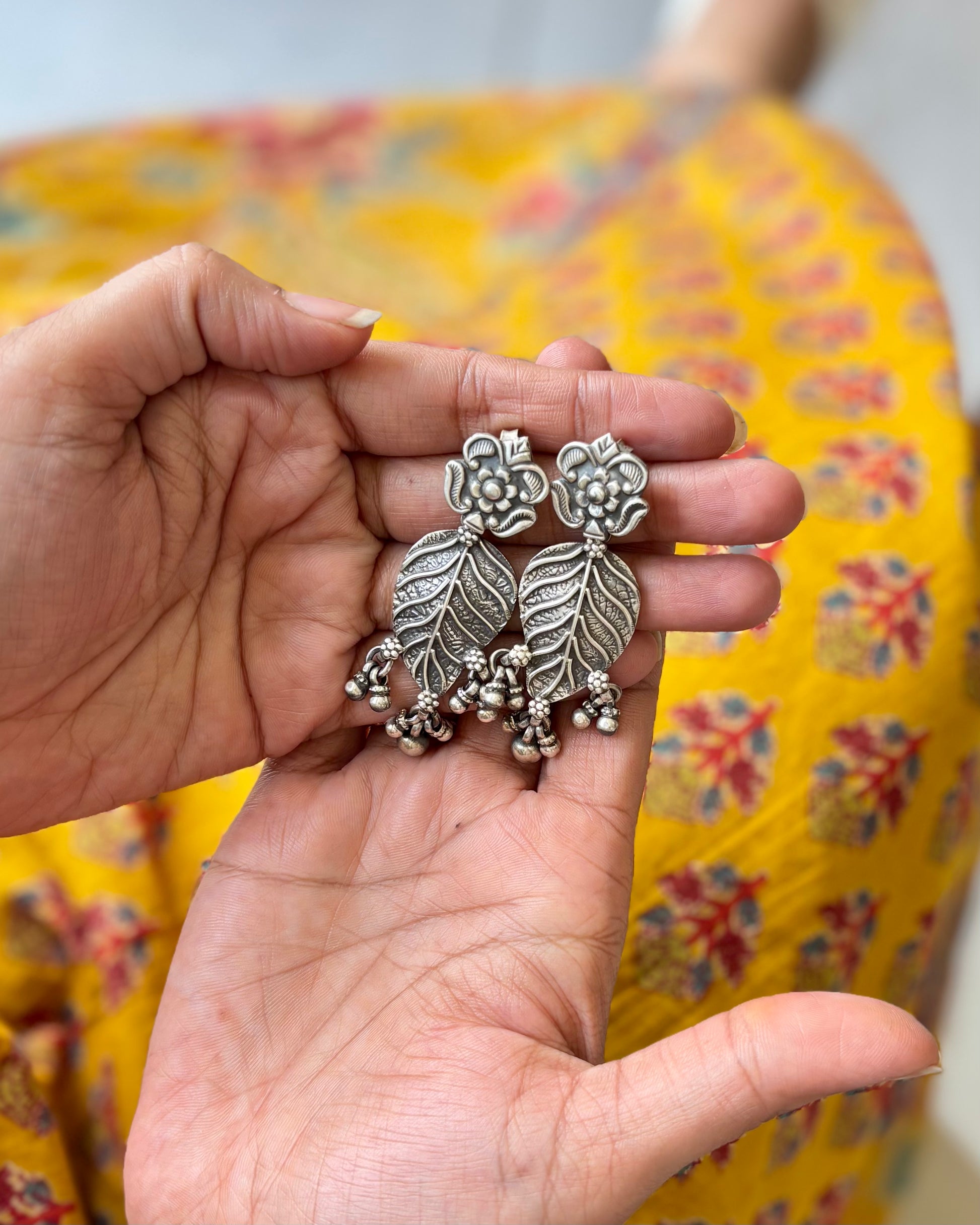 Hand holding a pair of silver floral earrings with a colorful fabric background