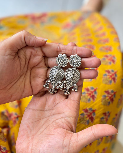 Hand holding a pair of silver floral earrings with a colorful fabric background