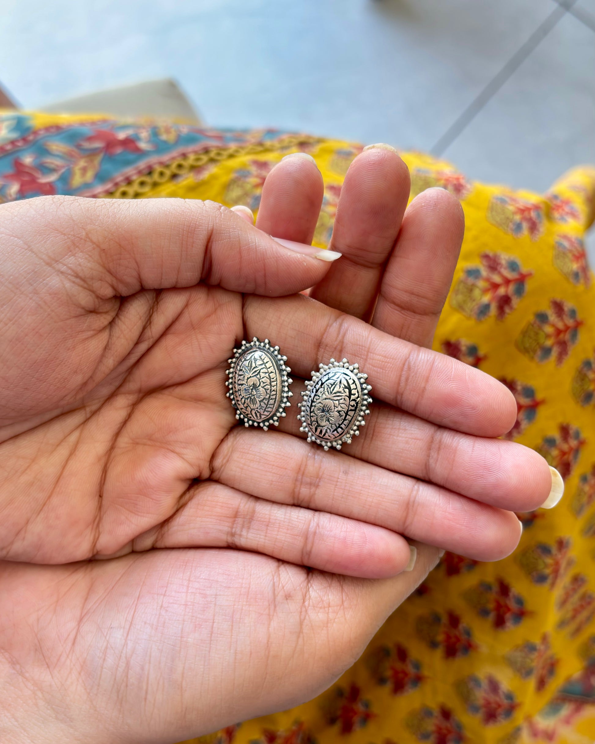 Silver earrings held in a hand with a colorful fabric background
