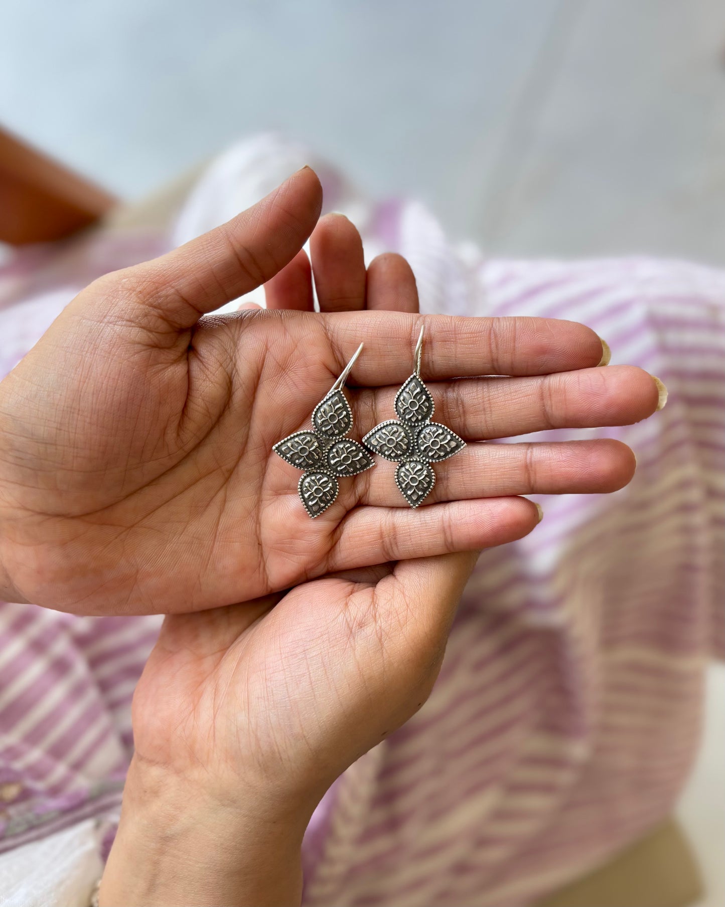 Hand holding a pair of silver earrings with a blurred background
