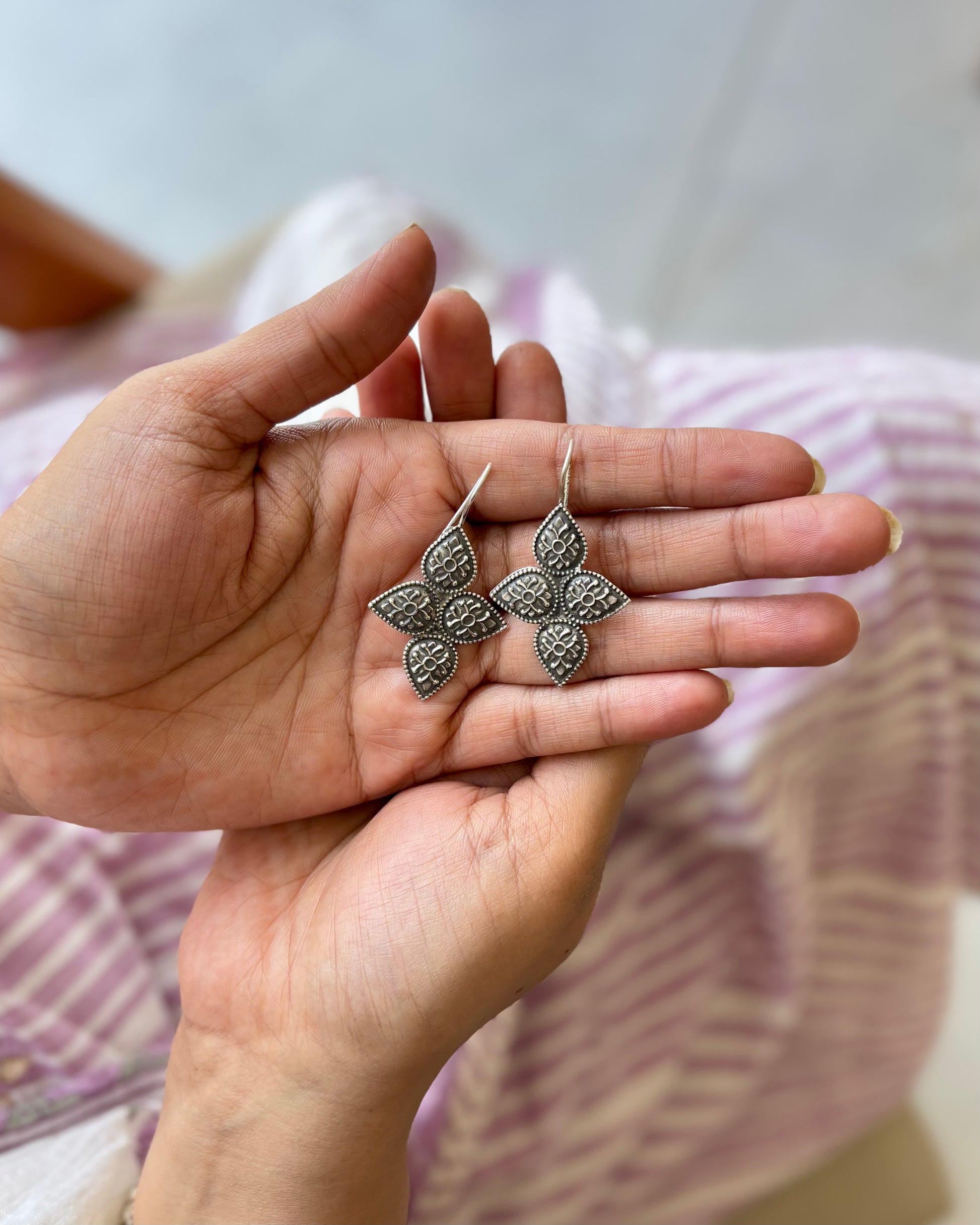 Hand holding a pair of silver earrings with a blurred background