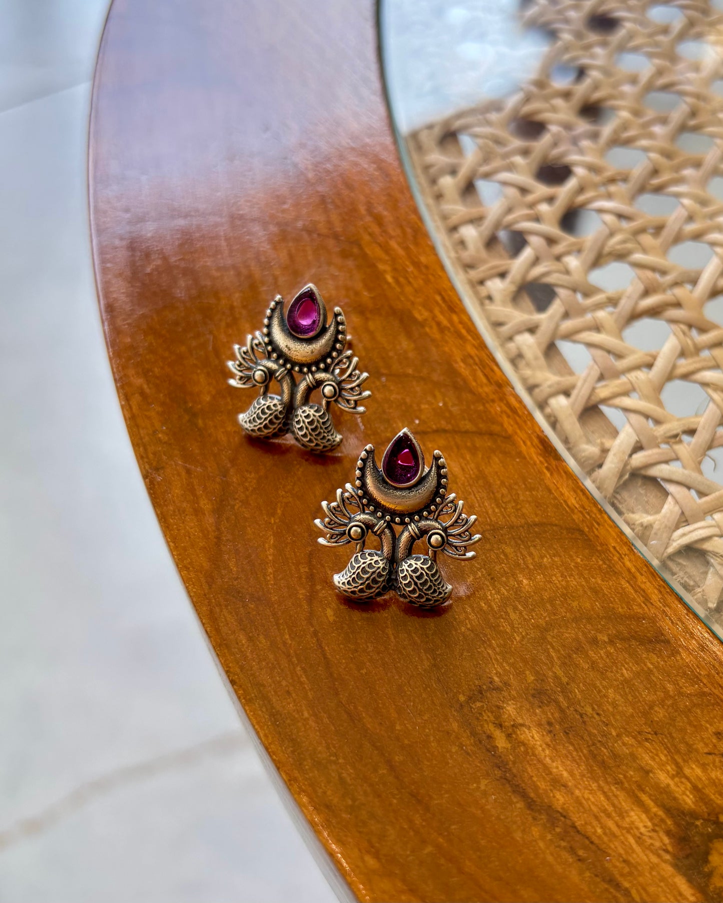 Pair of ornate earrings with red gemstones on a wooden surface