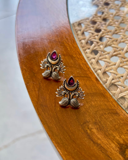 Pair of ornate earrings with red gemstones on a wooden surface