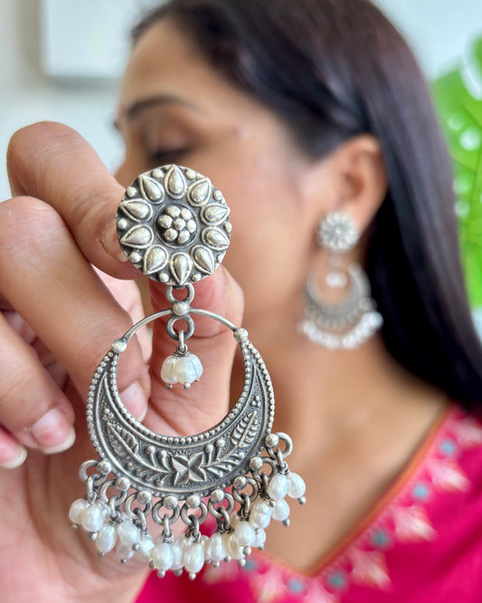 Silver earrings with floral design held by a hand, blurred background