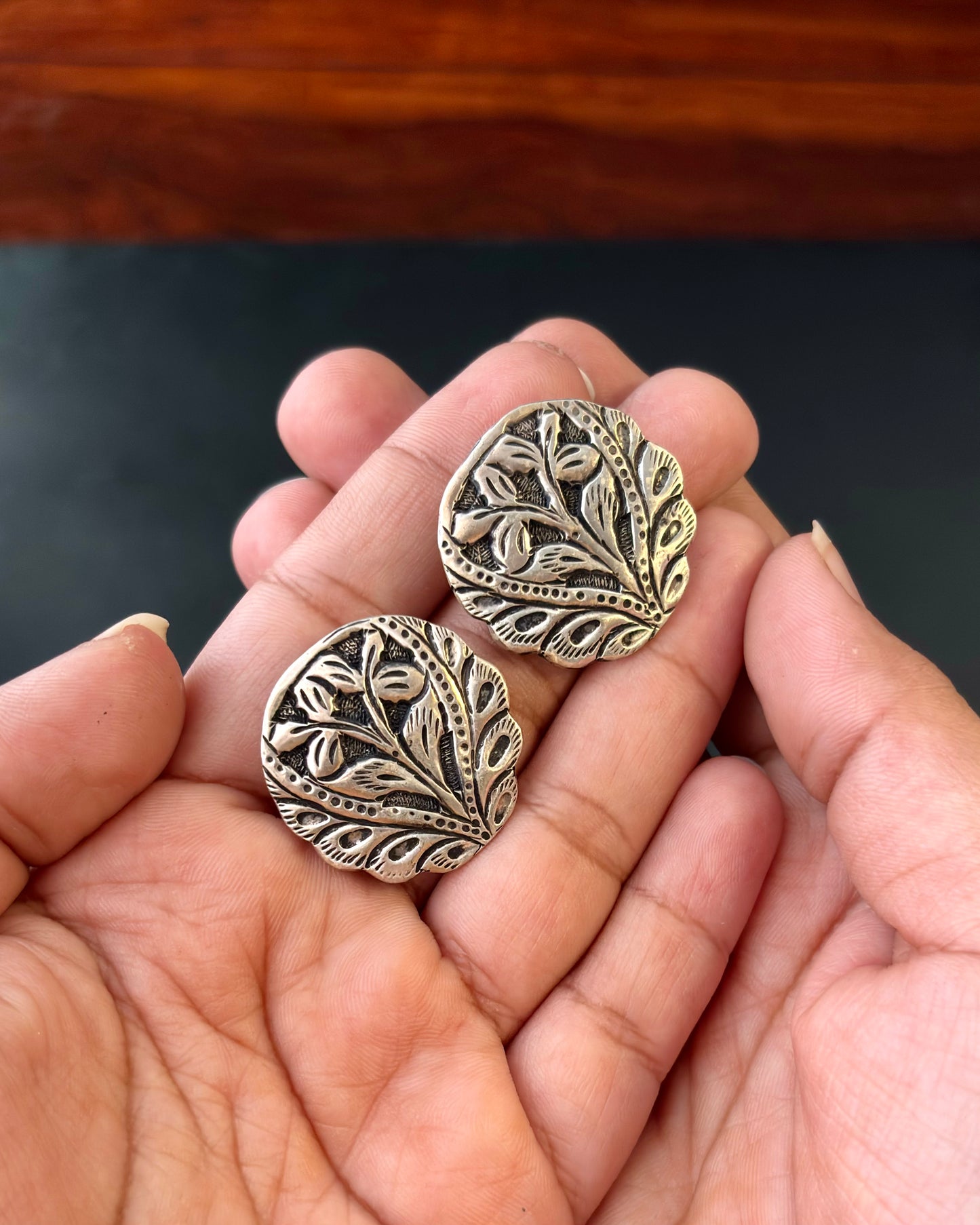 Two ornate silver earrings held in a hand against a dark background, 92.5 silver earrings