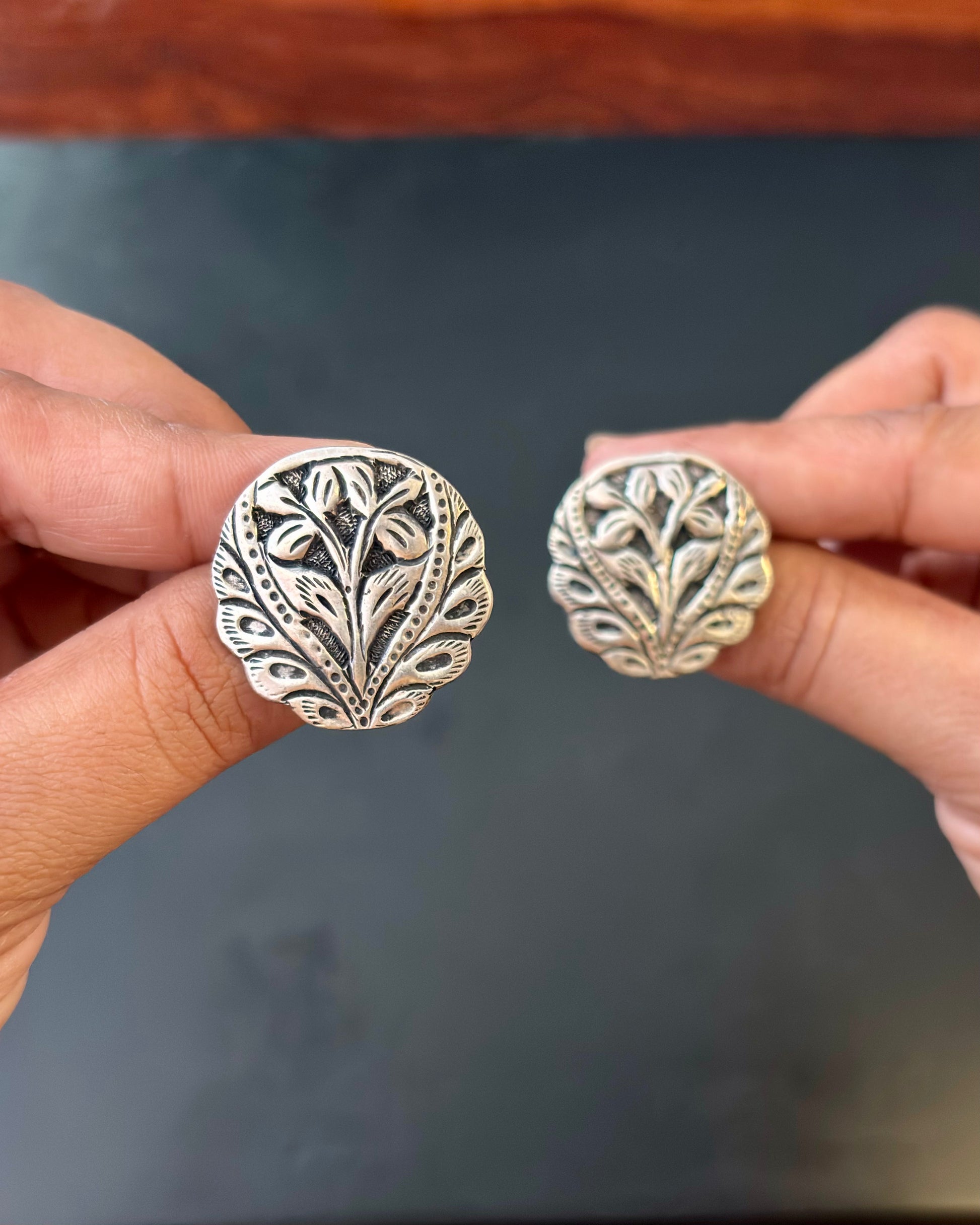 Silver leaf-patterned earrings held between fingers against a dark background, pure 92.5 silver earrings