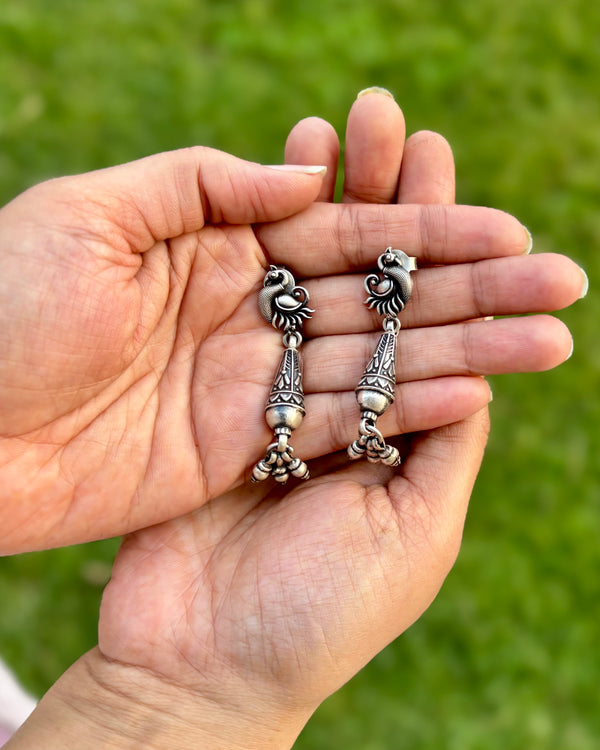 Hand holding a pair of silver earrings against a green background