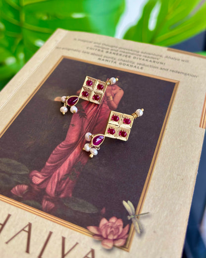 Gold earrings with red gemstones on a decorative card with floral design