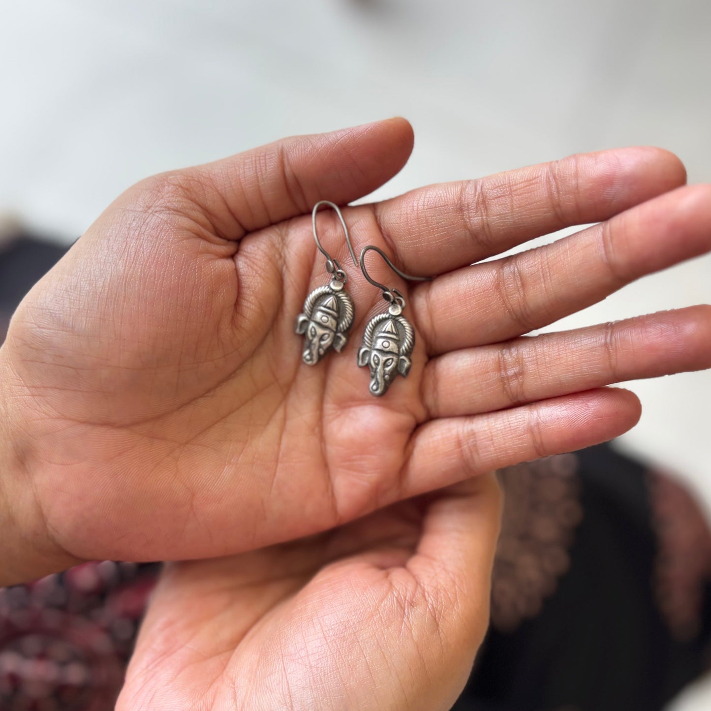Hand holding a pair of silver earrings with a blurred background