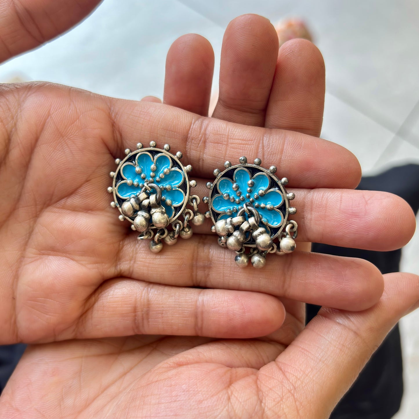Silver earrings with blue floral designs held in a hand.